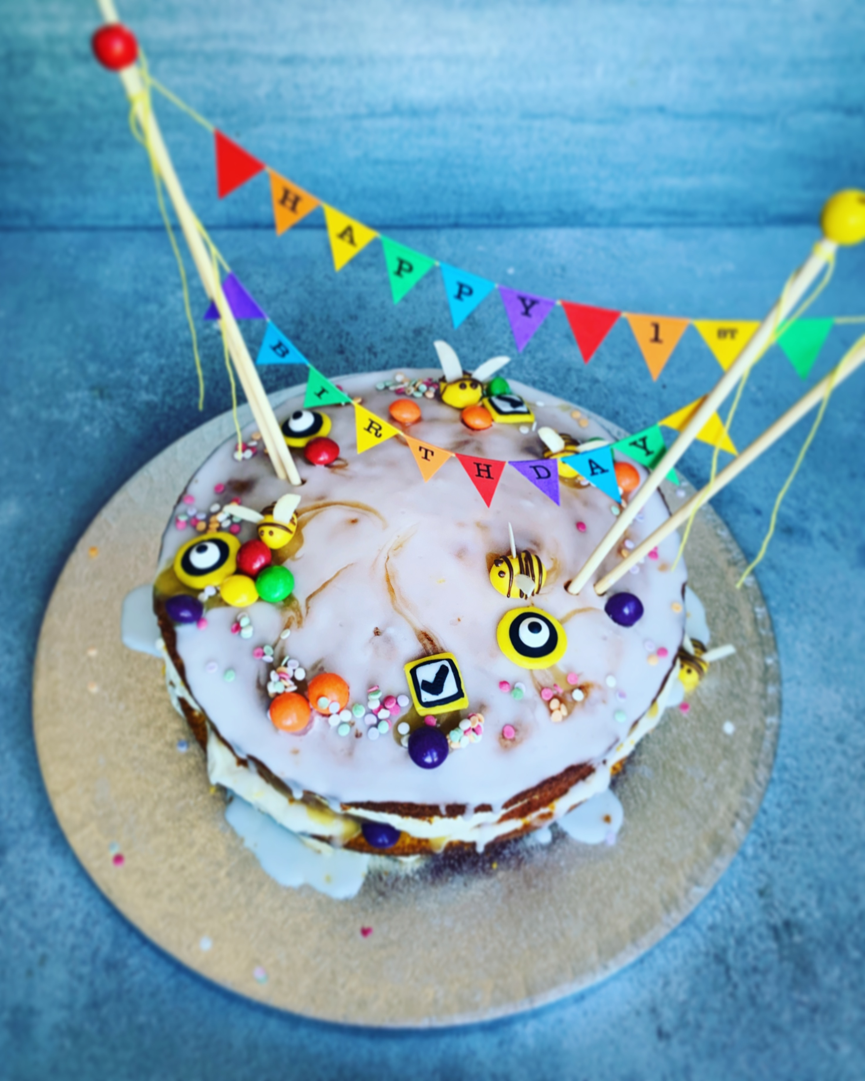 An iced cake topped with bunting and fondant radio buttons, checkboxes, bumble bees and sprinkles
